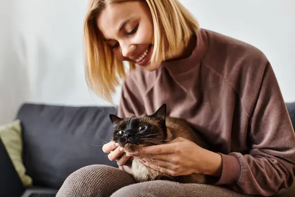 Una donna con i capelli corti siede pacificamente su un divano, accarezzando il suo gatto. — Foto stock