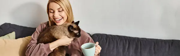 Una donna con i capelli corti si rilassa su un divano, culla il suo gatto tra le braccia, godendo di un momento di pace a casa. — Foto stock