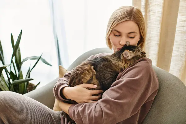Uma mulher com cabelo curto sentado em um sofá, embalando um gato em seus braços em um ambiente acolhedor e tranquilo. — Fotografia de Stock