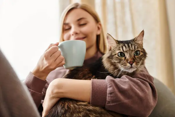 Una mujer con el pelo corto se sienta en un sofá acogedor, tiernamente sosteniendo a su gato en un momento de paz en casa. - foto de stock
