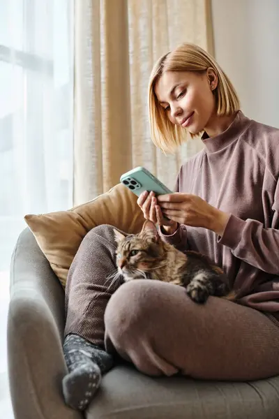 Una donna con i capelli corti che si rilassa su un divano mentre tiene affettuosamente il suo gatto. — Foto stock