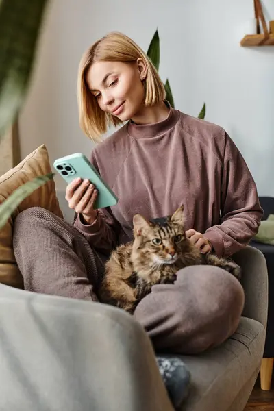 Uma mulher atraente com cabelo curto senta-se em um sofá, segurando seu gato em um momento pacífico e íntimo em casa. — Fotografia de Stock