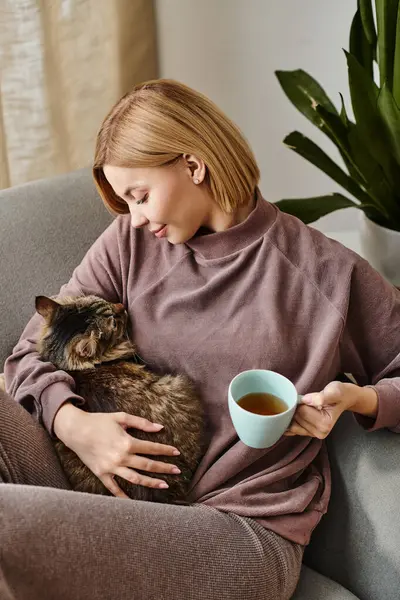 Eine Frau mit kurzen Haaren entspannt sich auf einer Couch und hält ihre Katze zärtlich in einem friedlichen Moment der Zuneigung und Gemeinschaft. — Stockfoto