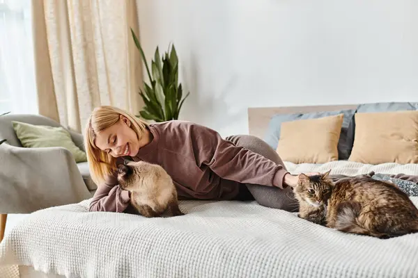 Сцена жінки з коротким волоссям, що розслабляється на ліжку поруч з її двома грайливими кішками. — стокове фото
