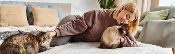 Eine Frau mit kurzen Haaren entspannt auf einem Bett, umgeben von zwei zufriedenen Katzen. — Stockfoto