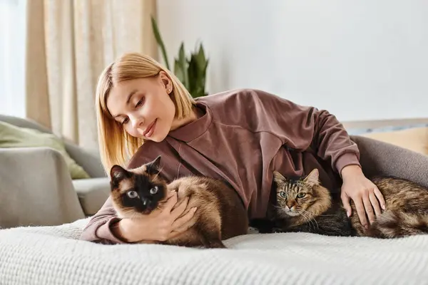 Una mujer con el pelo corto relajándose en una cama, acompañada de dos gatos cariñosos. - foto de stock