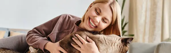 Una mujer serena con el pelo corto sentado en un sofá, tiernamente sosteniendo y abrazando a su amado gato. — Stock Photo