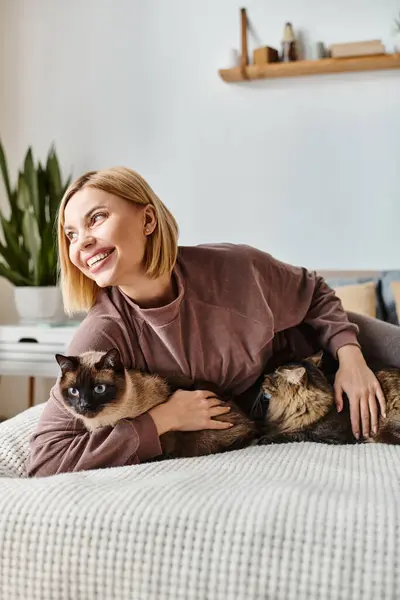 Una mujer con el pelo corto se relaja en una cama, abrazándose con un gato en un momento sereno de compañía. - foto de stock