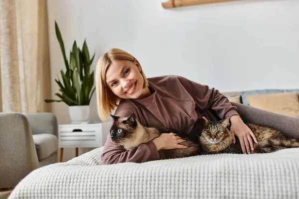 Uma mulher com cabelo curto relaxando em uma cama, abraçando dois gatos em casa em um momento de paz. — Fotografia de Stock