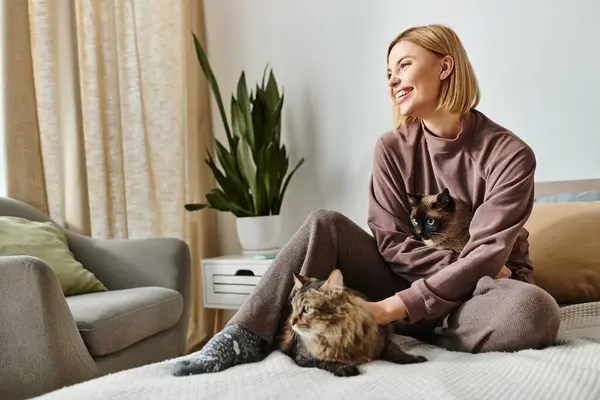 Une femme aux cheveux courts se détend sur un lit, entourée de deux chats câlins. — Photo de stock