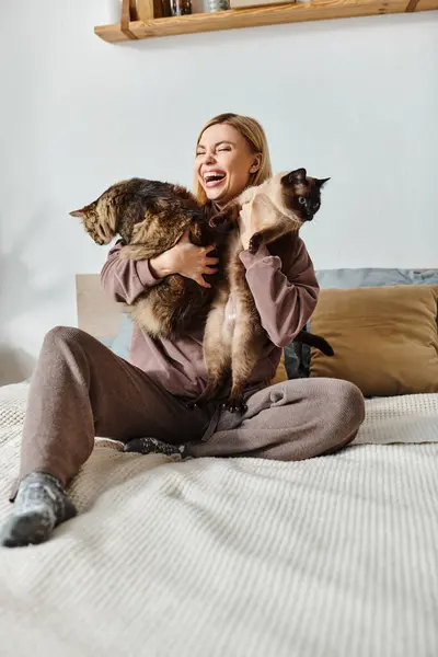 Une femme aux cheveux courts s'assoit paisiblement sur un lit, tenant deux chats près d'elle. — Photo de stock