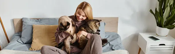 Una mujer con estilo se relaja en una cama con dos gatos, disfrutando de momentos de paz juntos en casa. - foto de stock