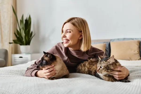 Una mujer con el pelo corto se relaja en una cama con dos gatos a su lado, disfrutando de un momento tranquilo en casa. - foto de stock
