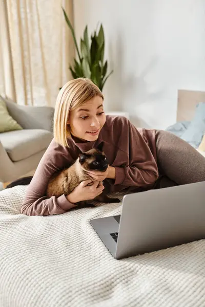 Uma mulher com cabelo curto relaxa em sua cama, acompanhada por seu gato e um laptop. — Fotografia de Stock