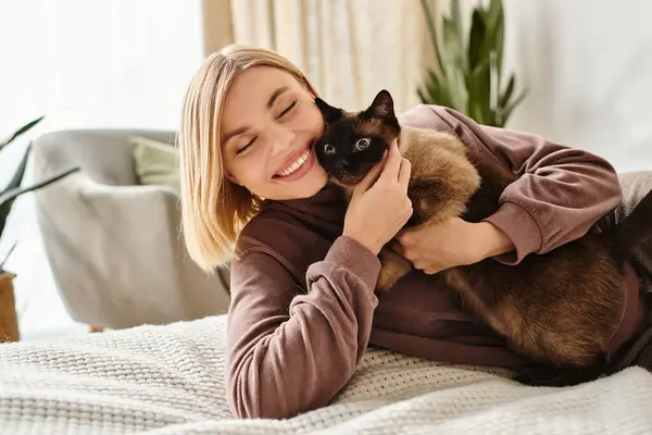 Una mujer con el pelo corto acostada en una cama, sosteniendo pacíficamente a su gato en un abrazo reconfortante. - foto de stock