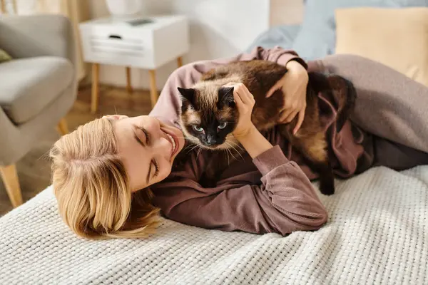 Жінка з коротким волоссям лежить на ліжку, ласкаво погладжуючи кота. — стокове фото