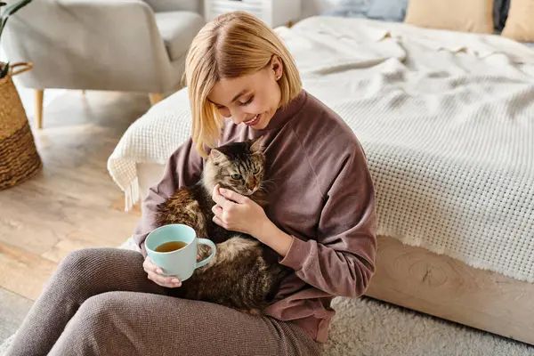 A serene woman with short hair sitting on the floor, affectionately holding her cat at home. — Stock Photo