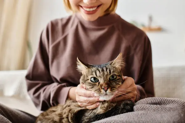 Una mujer se relaja en un sofá, su pelo corto enmarcando su cara mientras sostiene un gato contenido en sus brazos. - foto de stock