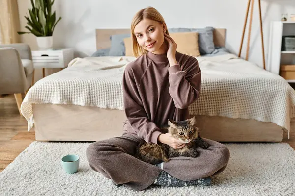 Una mujer con el pelo corto se sienta tranquilamente en el suelo, uniéndose con su gato en la comodidad de su casa. - foto de stock