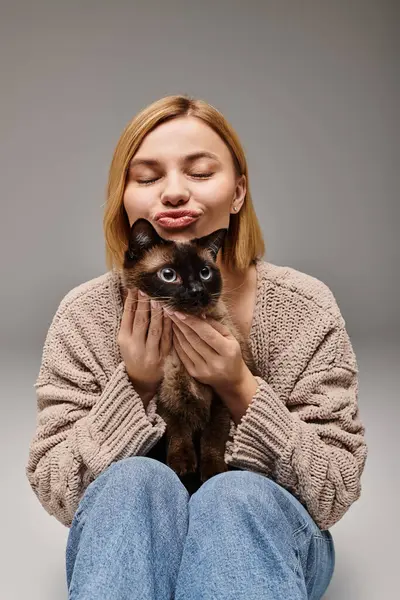 Une femme captivante, aux cheveux courts, s'assoit sur le sol tenant amoureusement un chat dans un cadre confortable. — Photo de stock