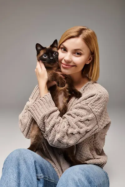 A woman with short hair comfortably sits on the floor, gently holding her cat in a peaceful and loving moment at home. — Stock Photo