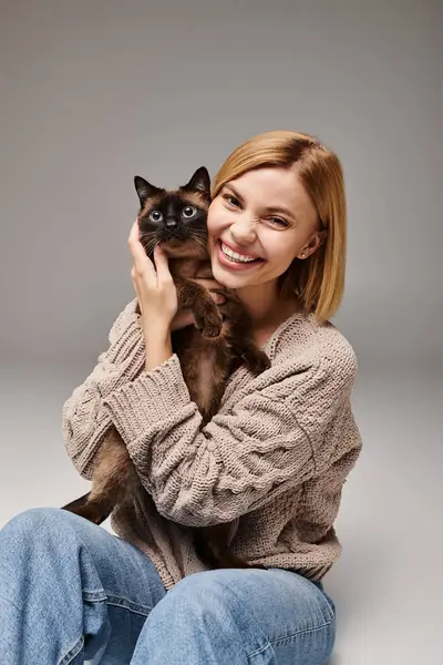 A woman with short hair sits on the floor, gently cradling a cat in her arms, forming a peaceful and loving bond. — Stock Photo
