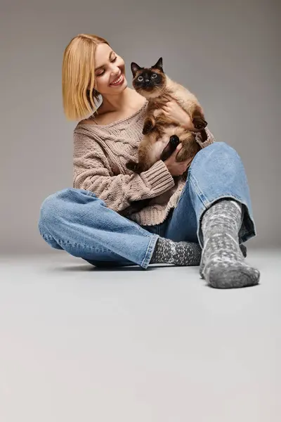 Une femme aux cheveux courts s'assoit par terre, tenant doucement son chat, partageant un moment de calme sérénité et d'admiration mutuelle. — Photo de stock