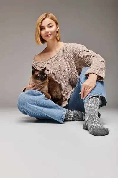 Una donna con i capelli corti seduta sul pavimento, che tiene amorevolmente il suo gatto mentre condivide un momento di connessione a casa. — Foto stock