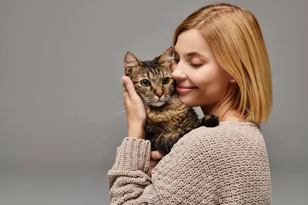 Uma mulher de cabelos curtos embalando suavemente um gato em suas mãos, mostrando amor e cuidado em um ambiente acolhedor em casa. — Fotografia de Stock