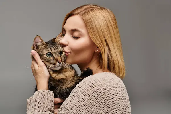 Una mujer de pelo corto acunando tiernamente a un gato en sus manos, formando un vínculo amoroso entre ellos en casa. - foto de stock