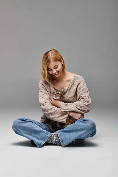 Una donna con i capelli corti siede sul pavimento, tenendo il suo gatto in un abbraccio amorevole in un ambiente accogliente casa. — Foto stock