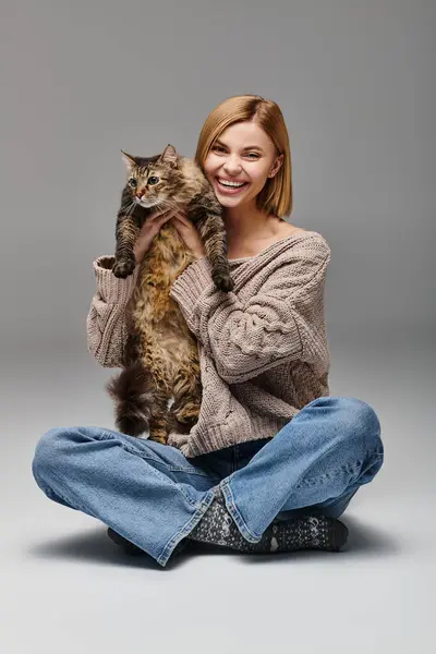 Una mujer con el pelo corto sentado en el suelo, acunando a su gato tiernamente en sus brazos, creando un ambiente sereno y tranquilo. - foto de stock