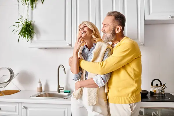 A mature, loving couple in cozy homewear standing together in their kitchen, enjoying each others company. — Stock Photo