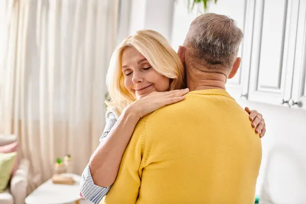 Una mujer madura en ropa de casa acogedora abraza a un hombre en un cálido abrazo amoroso en su sala de estar. - foto de stock