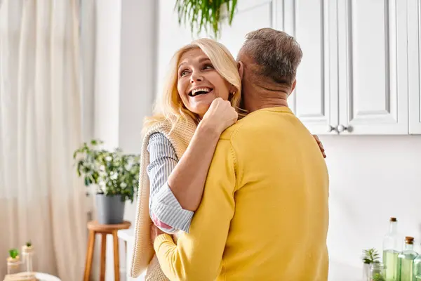 A mature loving couple in cozy homewear sharing a warm hug in the kitchen of their home. — Stock Photo