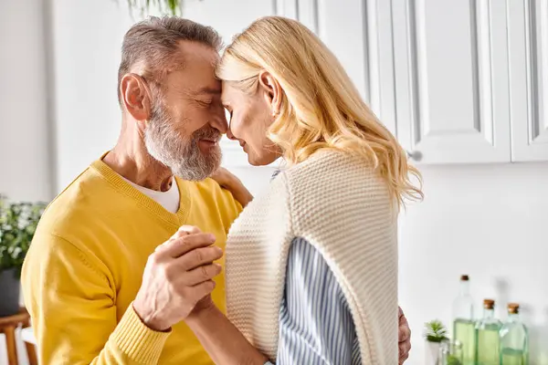Una coppia matura amorevole in accoglienti abiti da casa abbraccia nella loro cucina, condividendo un momento di intimità. — Foto stock