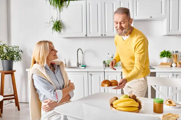 Un hombre y una mujer en ropa interior acogedora de pie juntos en una cocina, comprometidos en actividades amorosas y domésticas. - foto de stock