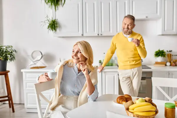 Un couple mature et aimant dans des vêtements confortables cuisine heureux ensemble dans leur cuisine à la maison, créant de délicieux plats avec des sourires. — Photo de stock
