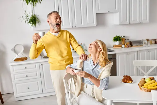 A mature loving couple, dressed in cozy homewear, standing together in a kitchen, engaged in cooking or conversation. — Stock Photo