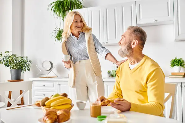 Una coppia matura amorevole in accogliente biancheria da casa seduta a un tavolo da cucina, godendo di un momento di intimità e connessione. — Foto stock