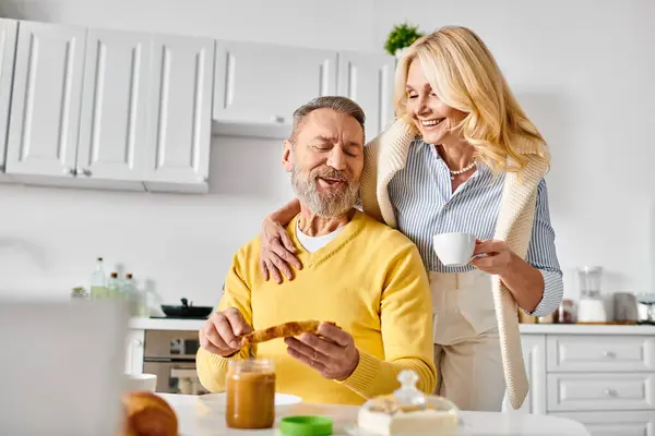 A mature man and woman in cozy home attire stand together in a warm kitchen, enjoying each others company. — Stock Photo