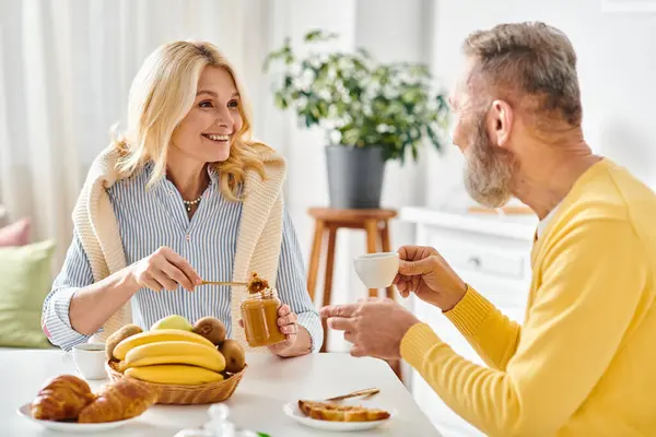 A mature loving couple in cozy homewear sitting at a table, enjoying a meal together in a warm and inviting kitchen. — Stock Photo
