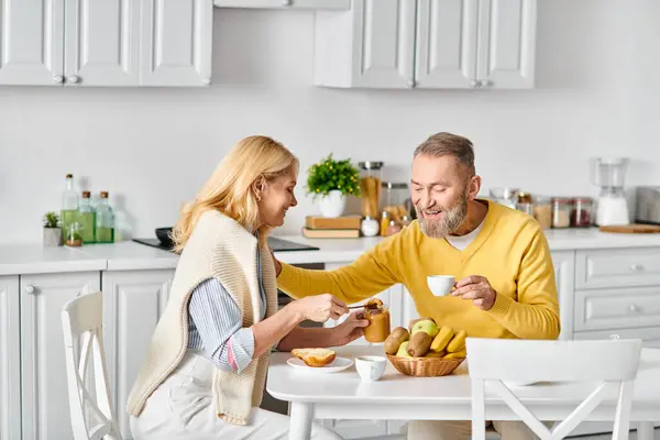 A mature, loving couple in cozy homewear enjoy a meal together at a table in their home. — Stock Photo
