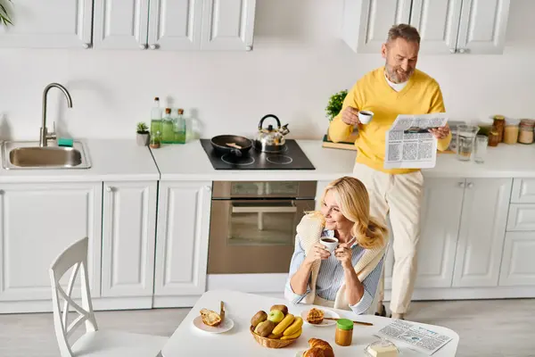 Una pareja madura y cariñosa en acogedora ropa de casa disfruta del tiempo juntos en la cocina en casa, compartiendo risas y preparando una comida.. - foto de stock