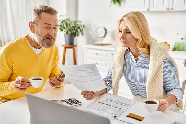 A mature man and woman in comfy attire sit at a table, engaged in reviewing and discussing paperwork together. — Stock Photo