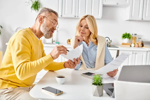A mature, loving couple in cozy homewear spending time together at a table filled with papers. — Stock Photo