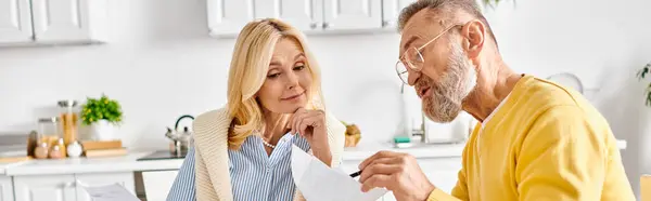 A mature loving couple in cozy homewear deeply engrossed in reading a piece of paper together in their kitchen at home. — Stock Photo