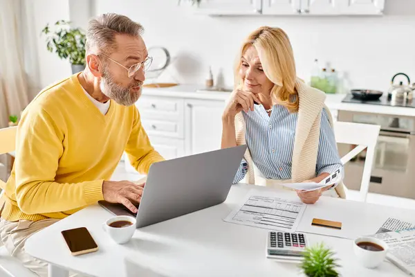 A mature man and woman in homewear sitting at a table, focused on a laptop screen. — Stock Photo