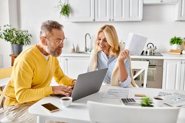 A mature man and woman, in homewear, sitting at a table, engrossed in the laptop screen before them. — Stock Photo