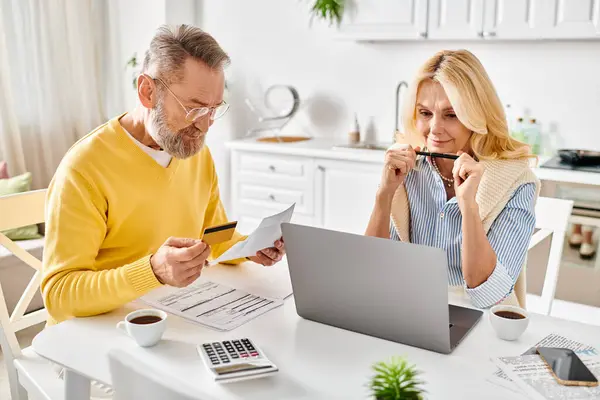 A mature couple in cozy homewear deeply engrossed in reviewing paperwork together at a table in their kitchen. — Stock Photo